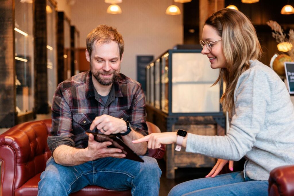 a man and a woman sitting on a couch looking at a tablet